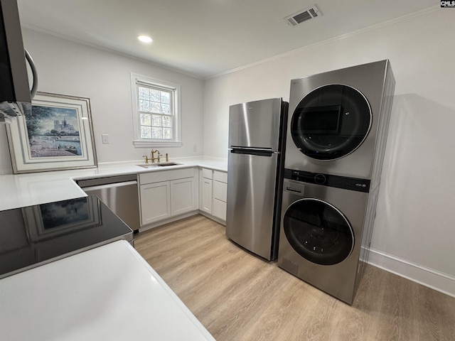 laundry room featuring light wood finished floors, stacked washing maching and dryer, a sink, and visible vents