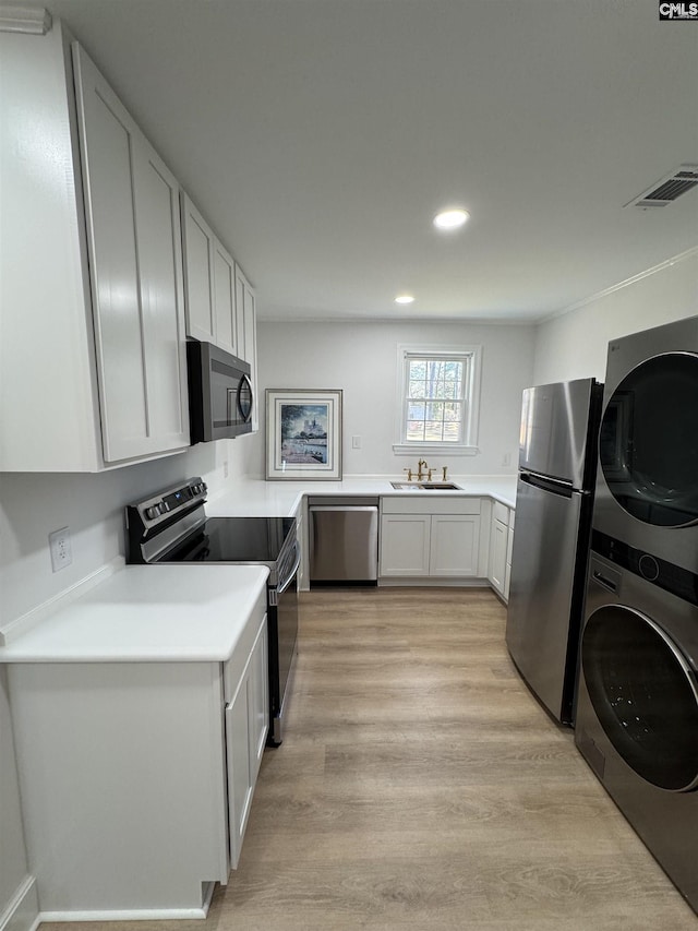 kitchen featuring light wood finished floors, stainless steel appliances, stacked washer and dryer, visible vents, and a sink