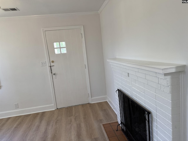 entryway featuring wood finished floors, visible vents, baseboards, a brick fireplace, and crown molding