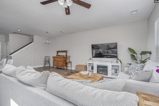 living area with visible vents, a glass covered fireplace, wood finished floors, and ceiling fan with notable chandelier