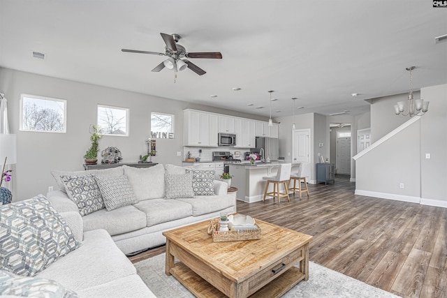 living area featuring ceiling fan with notable chandelier, visible vents, baseboards, and wood finished floors