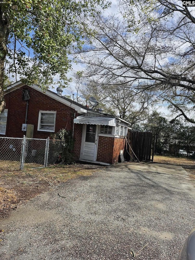 view of side of property featuring a gate, brick siding, fence, and driveway