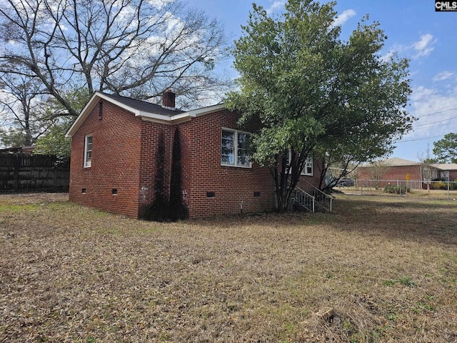 view of side of property with brick siding, fence, a yard, crawl space, and a chimney