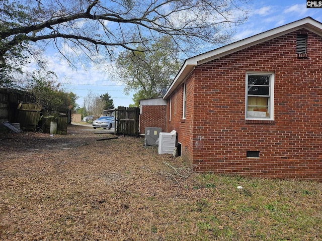 view of side of home featuring brick siding, crawl space, cooling unit, and fence