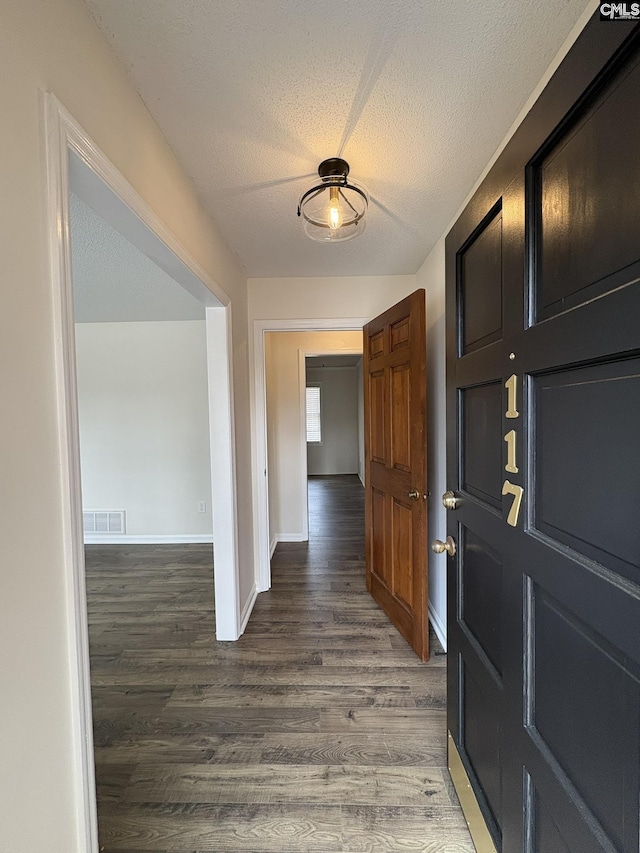 corridor with a textured ceiling, wood finished floors, visible vents, and baseboards