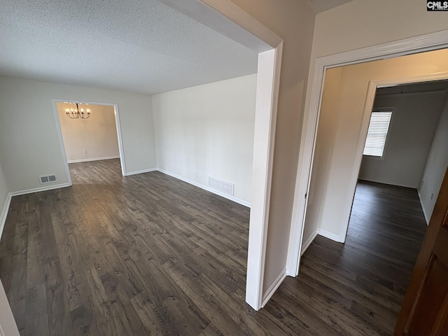 empty room with dark wood-style flooring, visible vents, a notable chandelier, and a textured ceiling