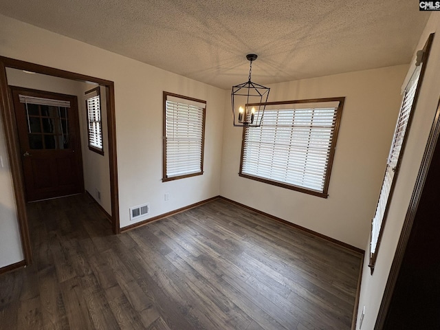 unfurnished dining area featuring a textured ceiling, dark wood finished floors, visible vents, and an inviting chandelier