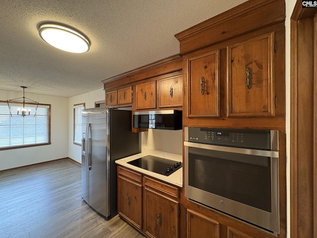 kitchen with appliances with stainless steel finishes, light wood-type flooring, brown cabinetry, and a textured ceiling