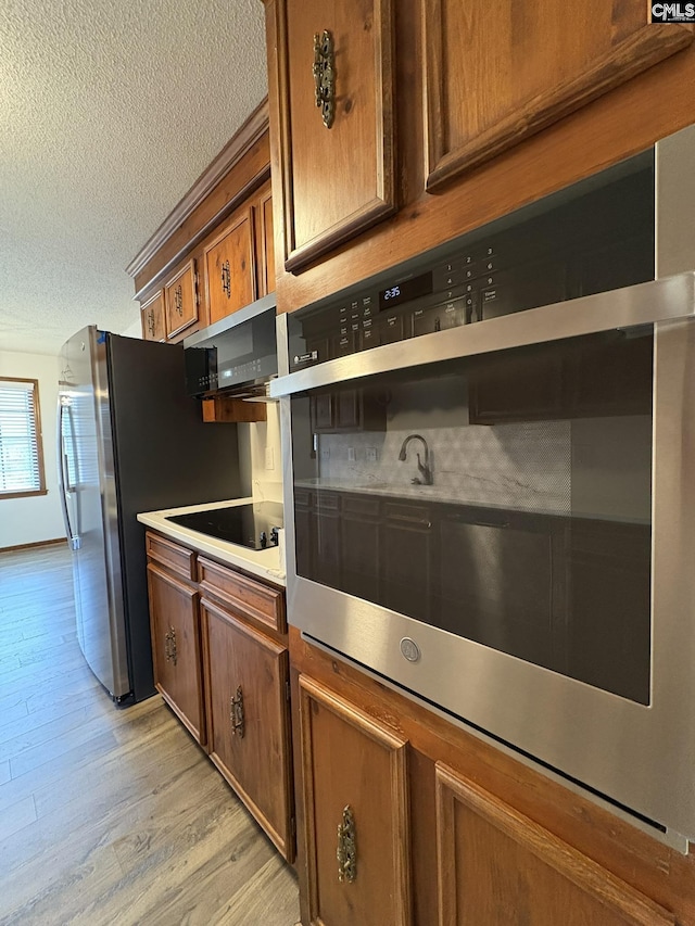 kitchen with brown cabinetry, light wood-style flooring, appliances with stainless steel finishes, light countertops, and a textured ceiling