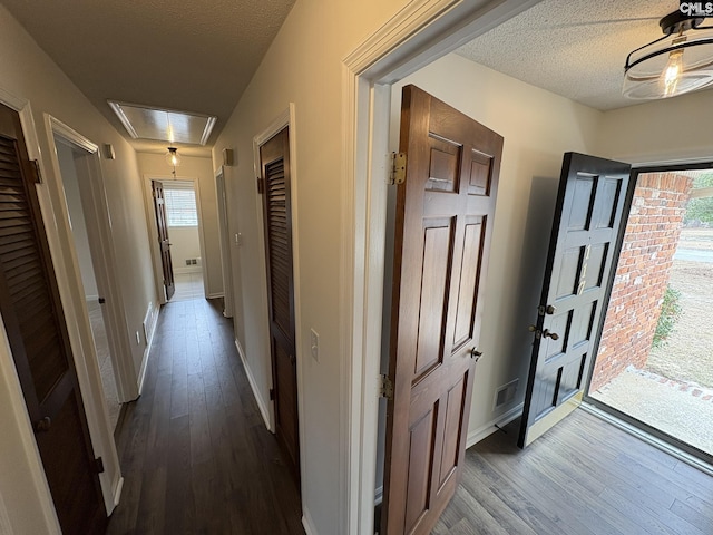 corridor with a textured ceiling, dark wood finished floors, attic access, and a healthy amount of sunlight