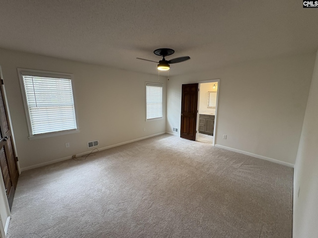 unfurnished bedroom featuring light colored carpet, visible vents, a ceiling fan, a textured ceiling, and baseboards