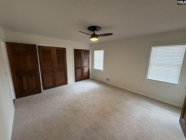 unfurnished bedroom with baseboards, a ceiling fan, carpet, a textured ceiling, and multiple closets