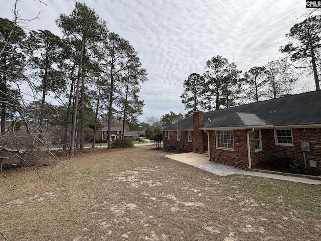 view of side of home with brick siding, a chimney, dirt driveway, central AC unit, and a patio area