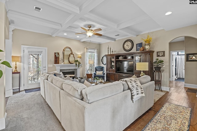 living area featuring arched walkways, beam ceiling, visible vents, a premium fireplace, and coffered ceiling