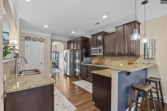 kitchen with arched walkways, appliances with stainless steel finishes, a sink, dark brown cabinetry, and a peninsula