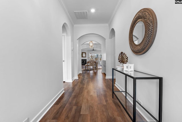 corridor featuring arched walkways, wood finished floors, visible vents, baseboards, and ornamental molding