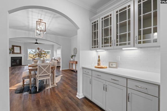 bar featuring dark wood-style flooring, crown molding, backsplash, a ceiling fan, and baseboards