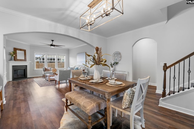 dining room with arched walkways, a fireplace with flush hearth, wood finished floors, baseboards, and stairs