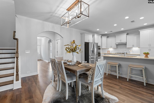 dining space featuring dark wood-style floors, arched walkways, recessed lighting, stairway, and ornamental molding