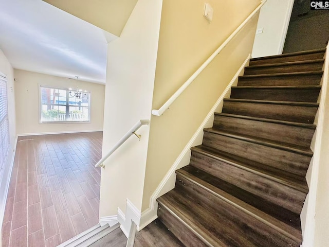 stairway featuring a chandelier, wood finished floors, and baseboards