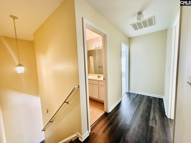 corridor with dark wood finished floors, visible vents, a sink, an upstairs landing, and baseboards