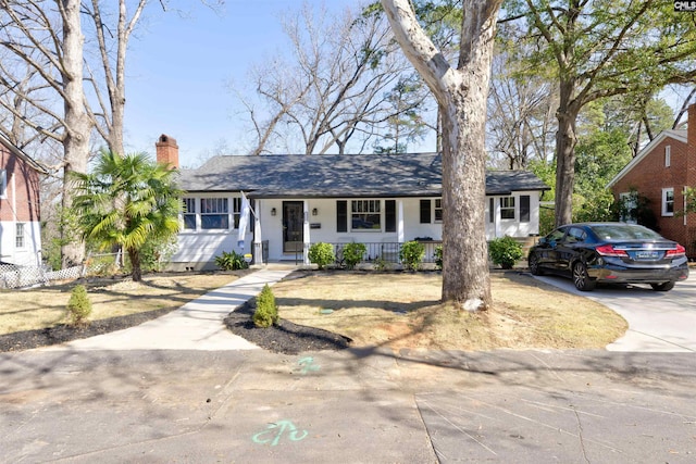 ranch-style home featuring covered porch, driveway, a chimney, and roof with shingles