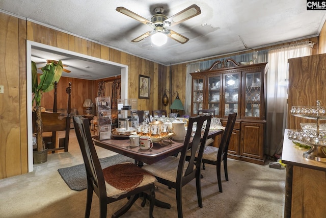 dining room with light colored carpet, ceiling fan, and wooden walls