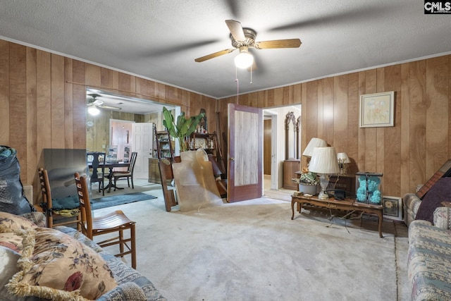 carpeted living area with a ceiling fan, wood walls, crown molding, and a textured ceiling