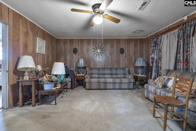 carpeted living room featuring a textured ceiling, wood walls, visible vents, and crown molding