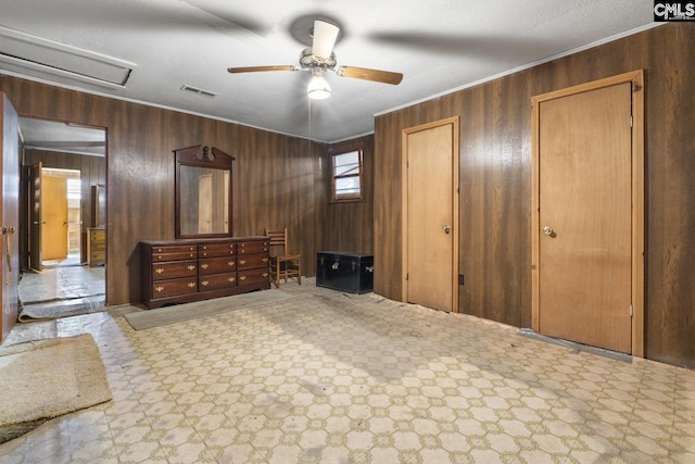 bedroom with wooden walls, a ceiling fan, visible vents, ornamental molding, and tile patterned floors