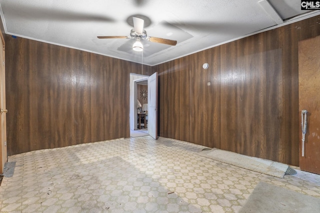 empty room with ceiling fan, wood walls, tile patterned floors, and crown molding