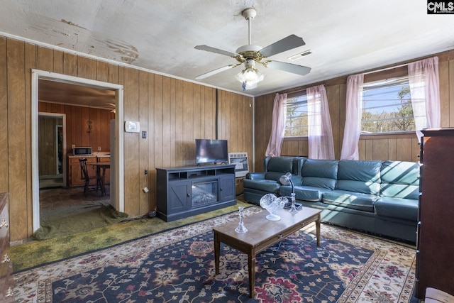 living area with wooden walls, visible vents, ceiling fan, carpet, and crown molding