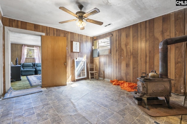 interior space with visible vents, ceiling fan, a wood stove, stairs, and wood walls