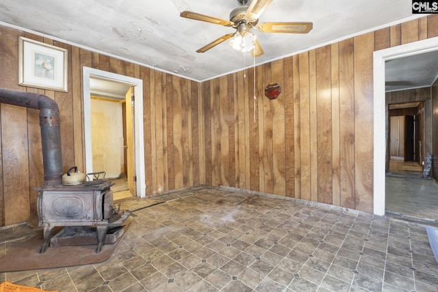 spare room with ceiling fan, wood walls, a wood stove, and crown molding