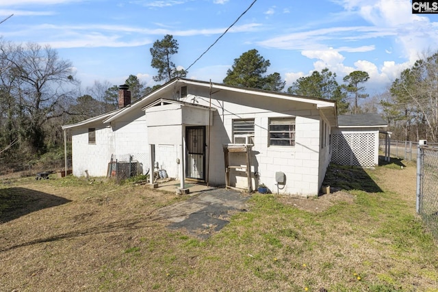 view of front of house with a chimney, fence, concrete block siding, and a front lawn