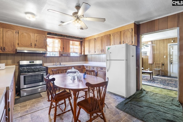 kitchen with stainless steel range with gas cooktop, light countertops, freestanding refrigerator, wooden walls, and under cabinet range hood