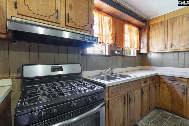 kitchen featuring brown cabinets, stainless steel gas range, light countertops, under cabinet range hood, and a sink