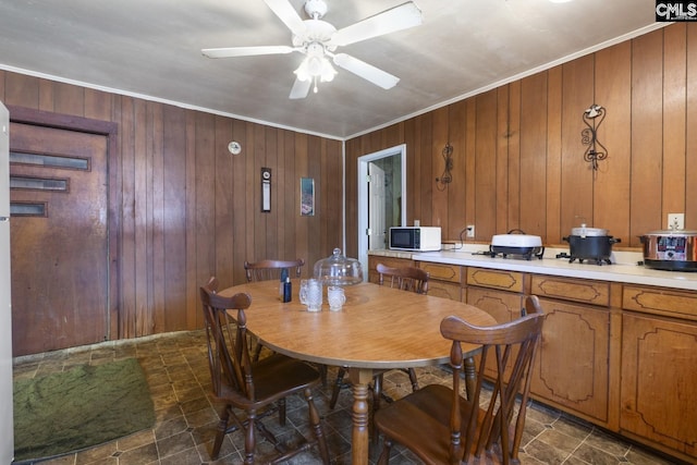 dining space with a ceiling fan, ornamental molding, and wooden walls