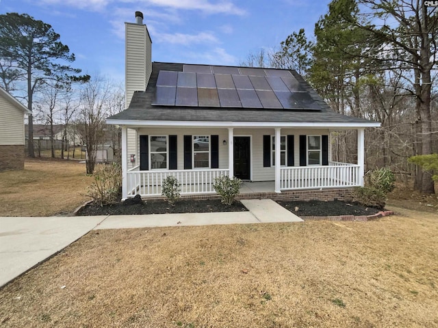 view of front facade featuring covered porch, roof mounted solar panels, a chimney, and a front yard