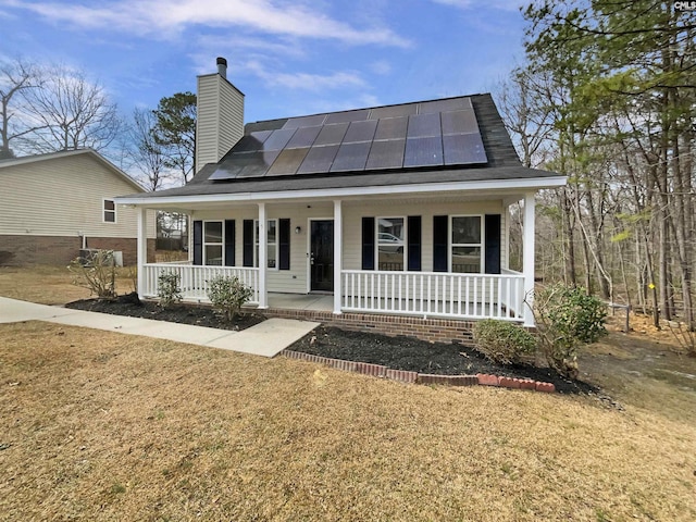 view of front of property with a standing seam roof, a porch, a chimney, and roof mounted solar panels