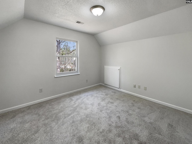 additional living space with a textured ceiling, carpet floors, visible vents, baseboards, and vaulted ceiling