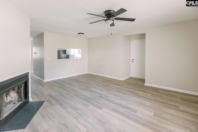 unfurnished living room with baseboards, ceiling fan, a multi sided fireplace, and wood finished floors