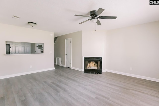 unfurnished living room with a fireplace with flush hearth, visible vents, baseboards, and wood finished floors