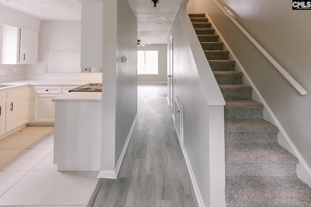 stairs featuring ceiling fan, baseboards, and a textured ceiling