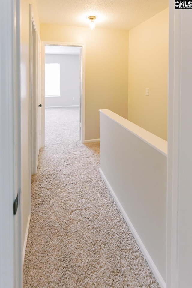 corridor featuring an upstairs landing, carpet flooring, a textured ceiling, and baseboards