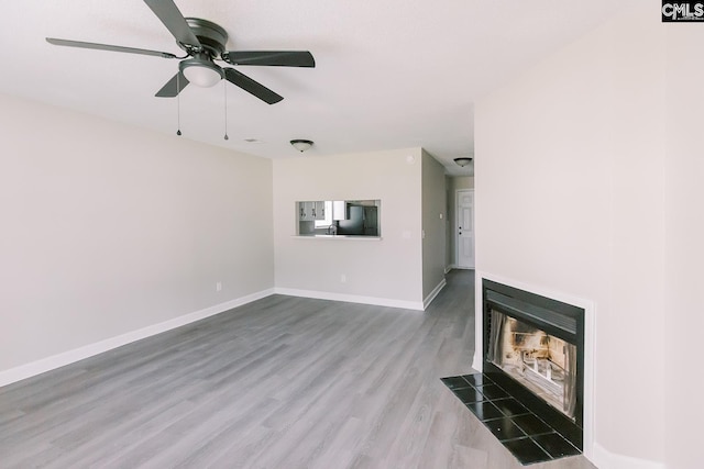 unfurnished living room featuring a fireplace with flush hearth, baseboards, ceiling fan, and wood finished floors