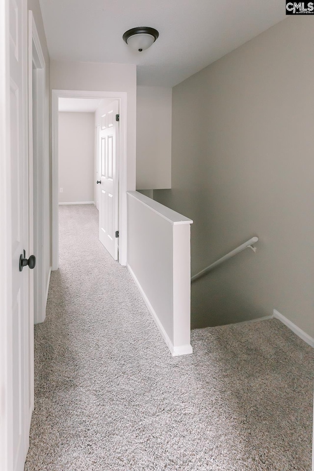 hallway featuring carpet flooring, an upstairs landing, and baseboards