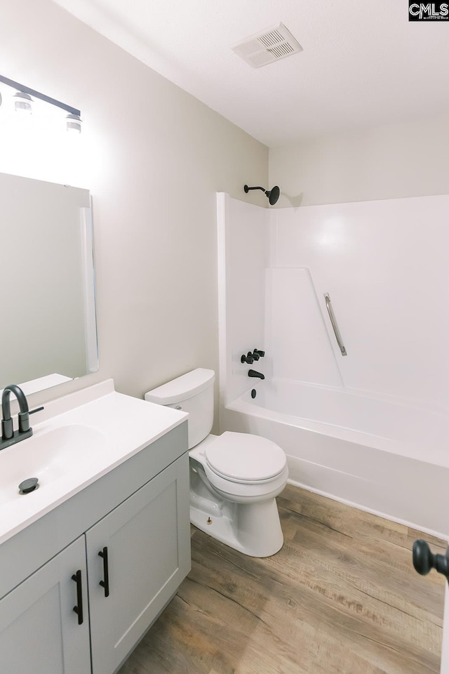 full bath featuring visible vents, shower / bathing tub combination, toilet, vanity, and wood finished floors