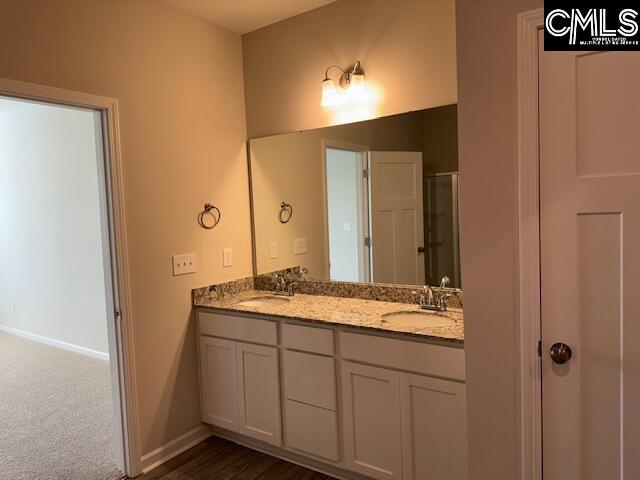 full bath featuring double vanity, a sink, a shower with shower door, and baseboards