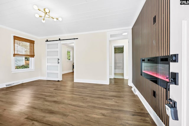 unfurnished living room with a barn door, wood finished floors, visible vents, baseboards, and ornamental molding